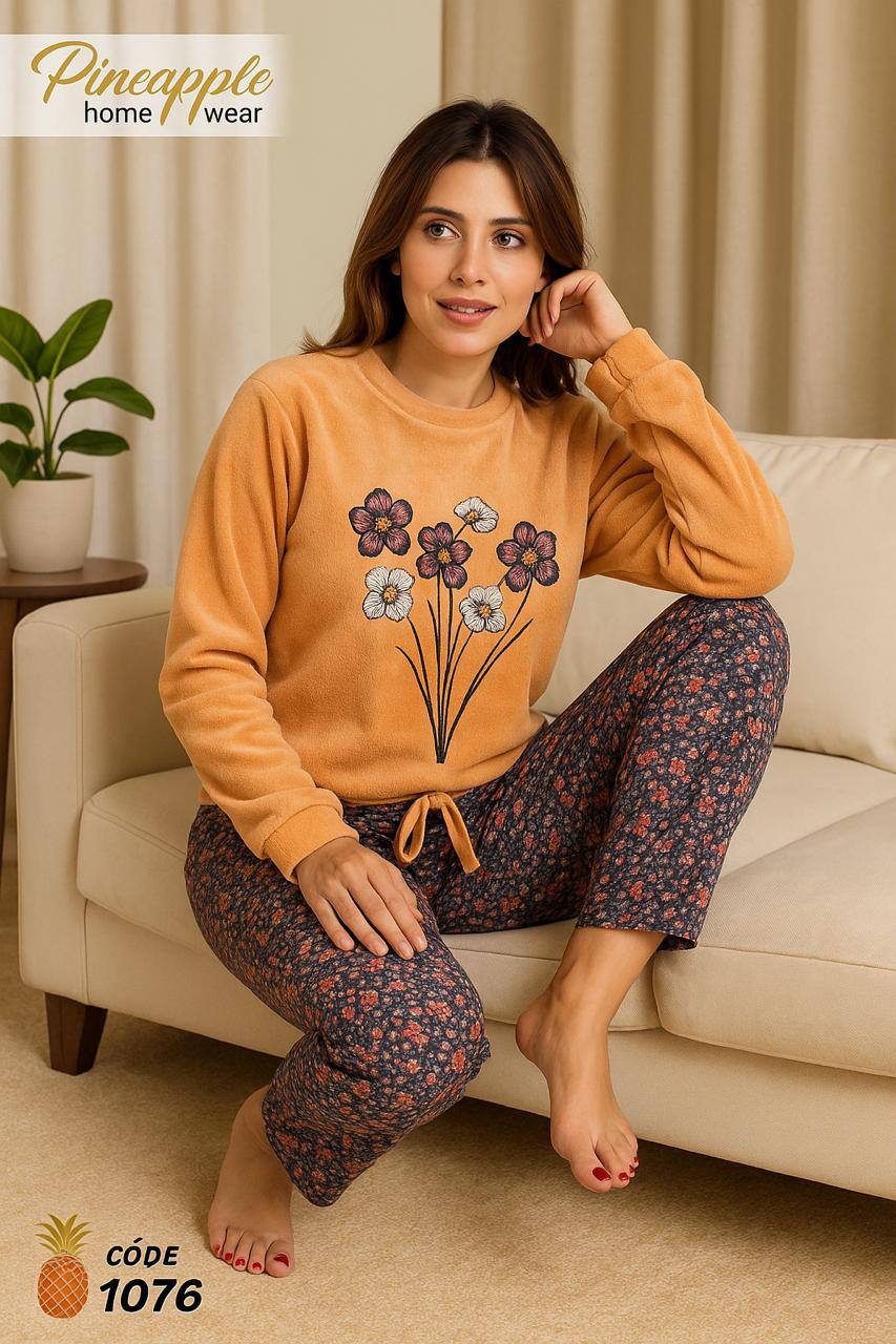 Woman wearing a mustard yellow sweatshirt with floral design and patterned pants sitting on a beige couch.