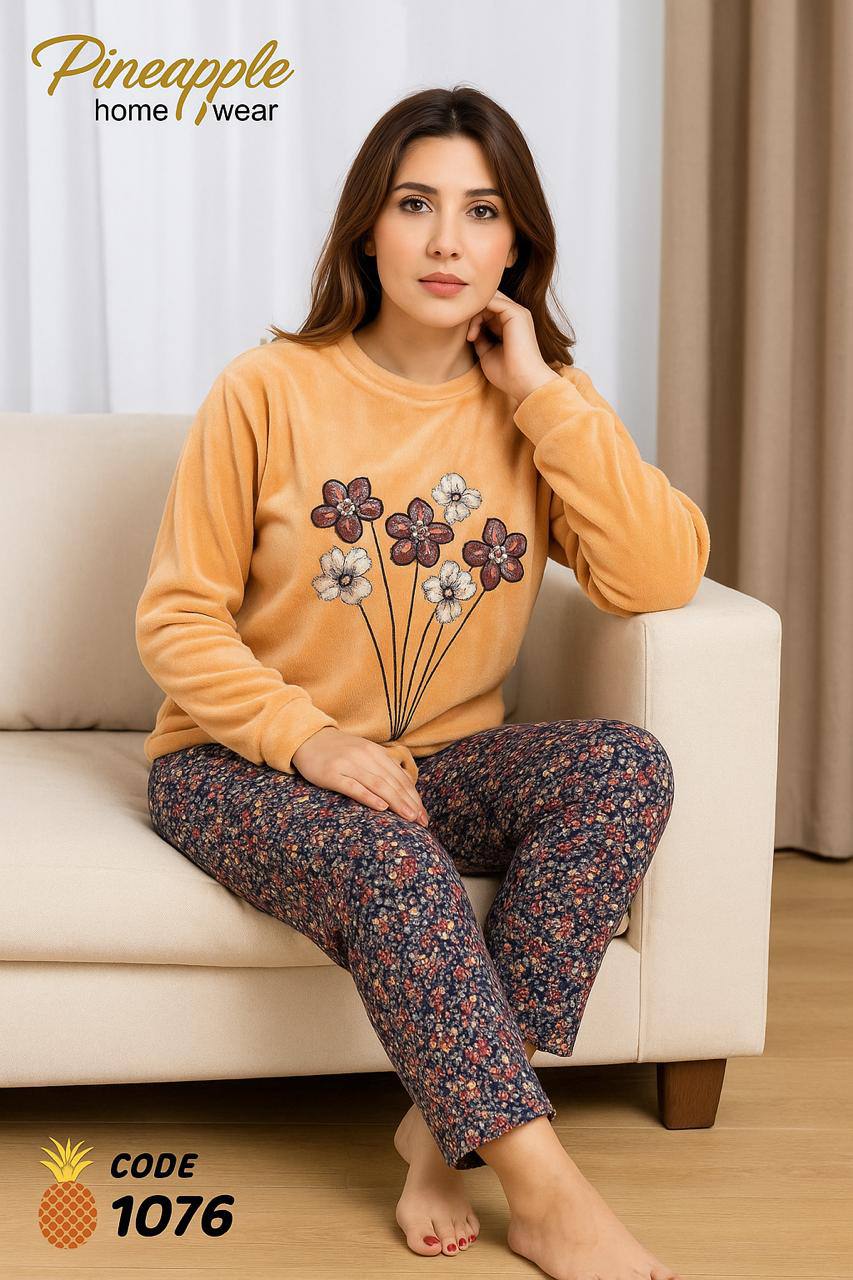 Woman sitting on a couch wearing a yellow sweater with floral design and patterned pants, branded as Pineapple home wear.