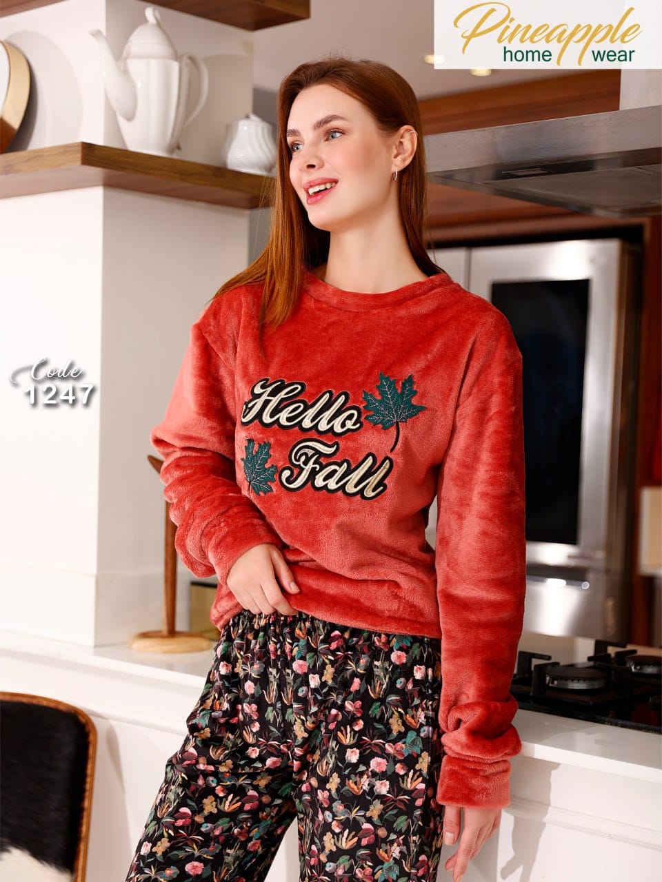 Woman wearing a red 'Hello Fall' sweater in a kitchen setting with 'Pineapple Home Wear' branding.
