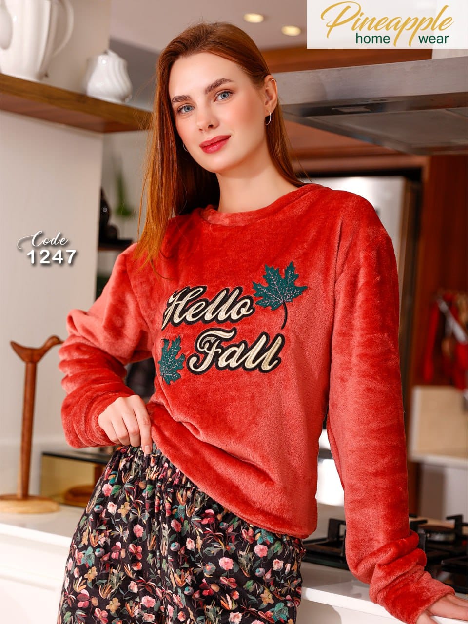 Woman wearing a red 'Hello Fall' sweater in a kitchen setting with 'Pineapple Home Wear' branding.