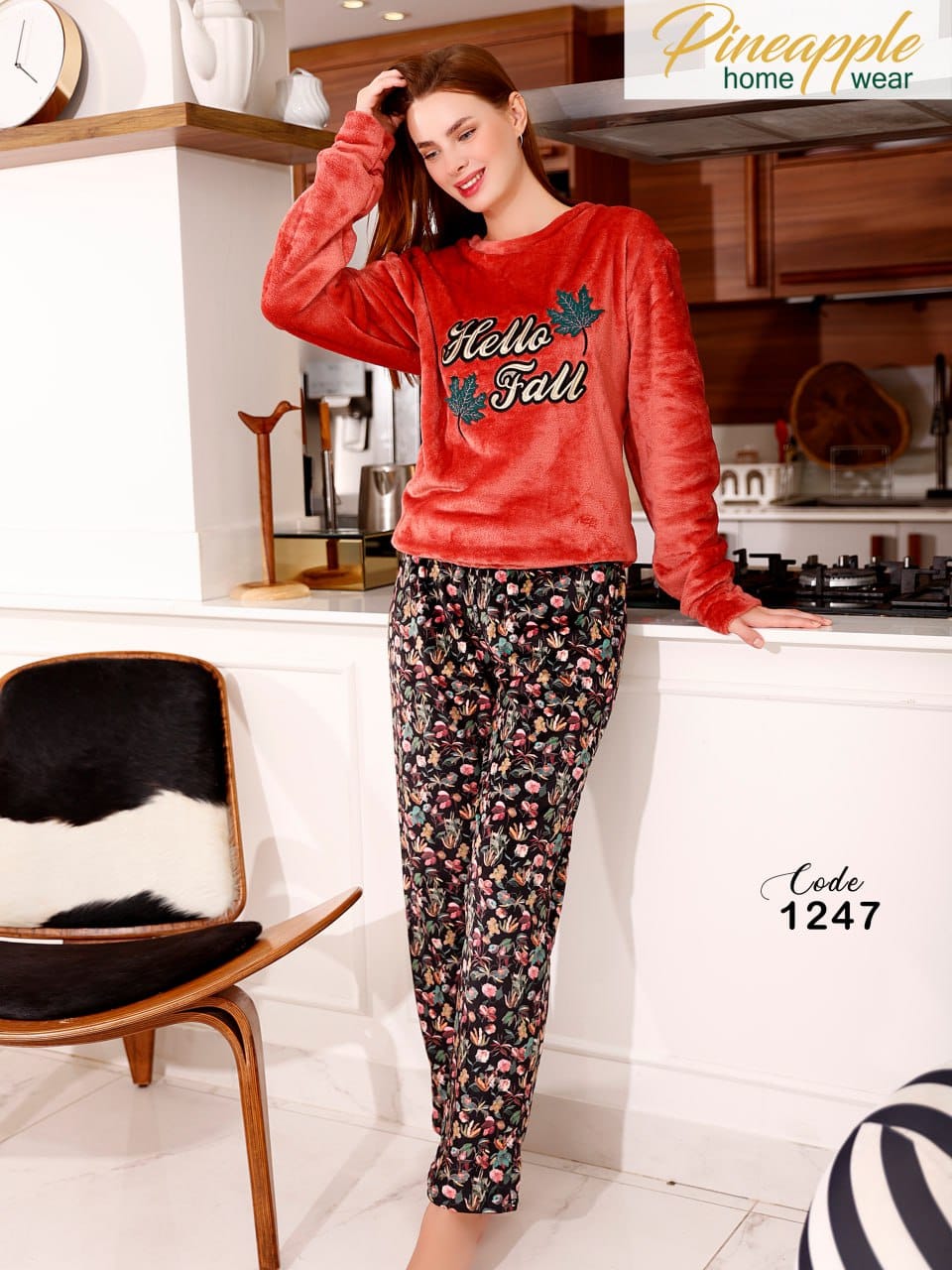 Woman wearing a red 'Hello Fall' sweatshirt and patterned pants in a kitchen setting, with 'Pineapple Home Wear' branding.