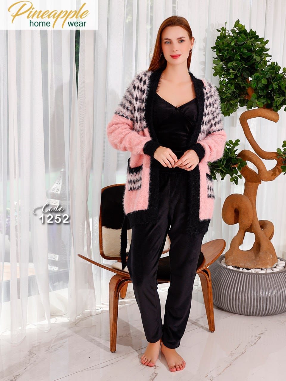 Woman wearing a black outfit with a pink and gray cardigan in a home setting.