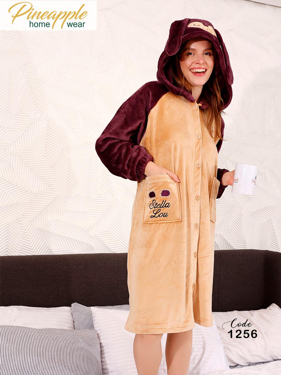 Person wearing a beige and maroon onesie with a hood, standing in a bedroom.