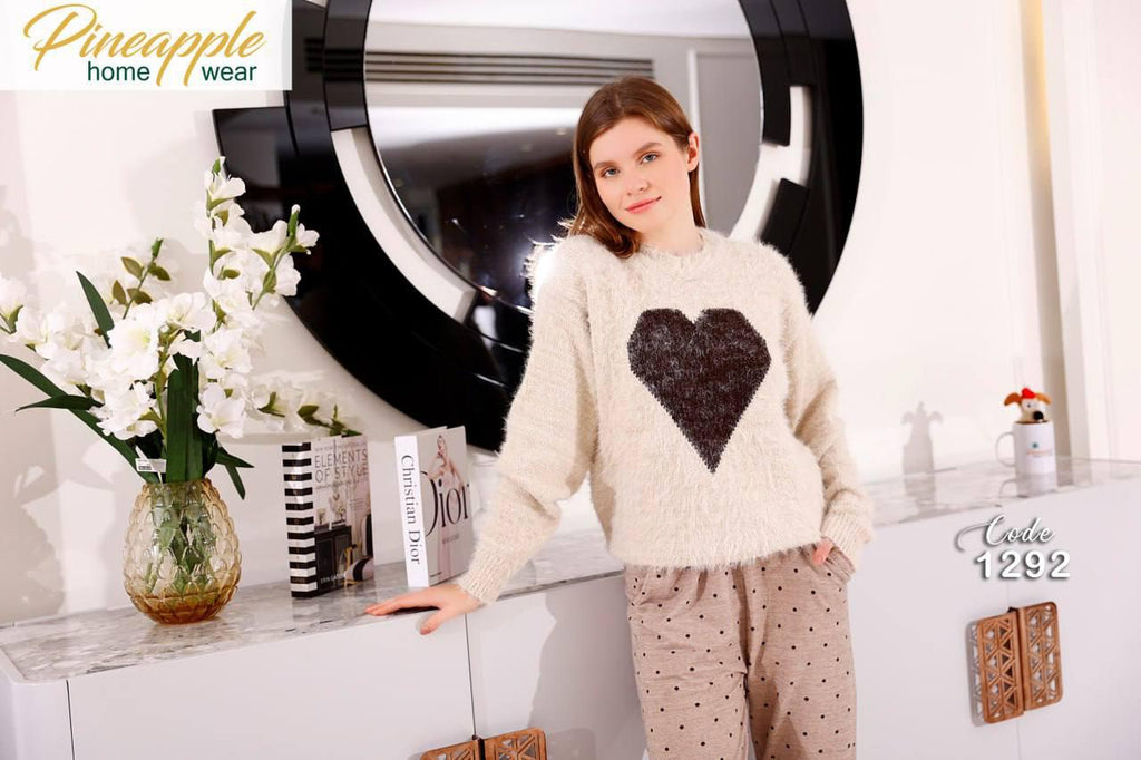 Woman wearing a white sweater with a black heart design in a home setting, with 'Pineapple Home Wear' branding.