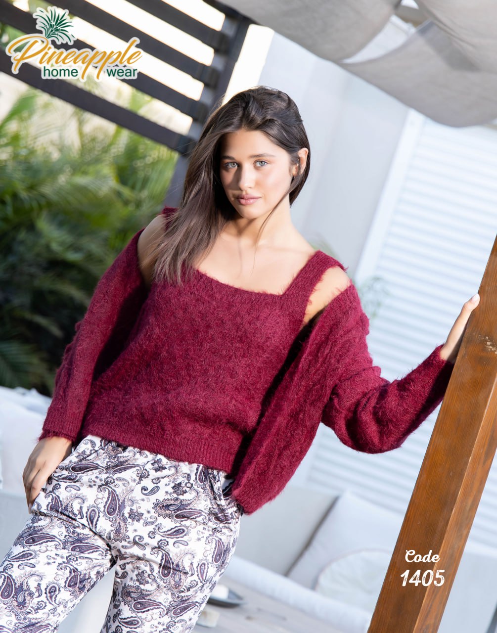 Woman wearing a maroon sweater and patterned pants, sitting on a chair with a blurred outdoor background.