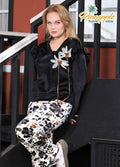 Woman sitting on stairs wearing a black top with floral details and patterned pants, with 'Pineapple Home Wear' logo.