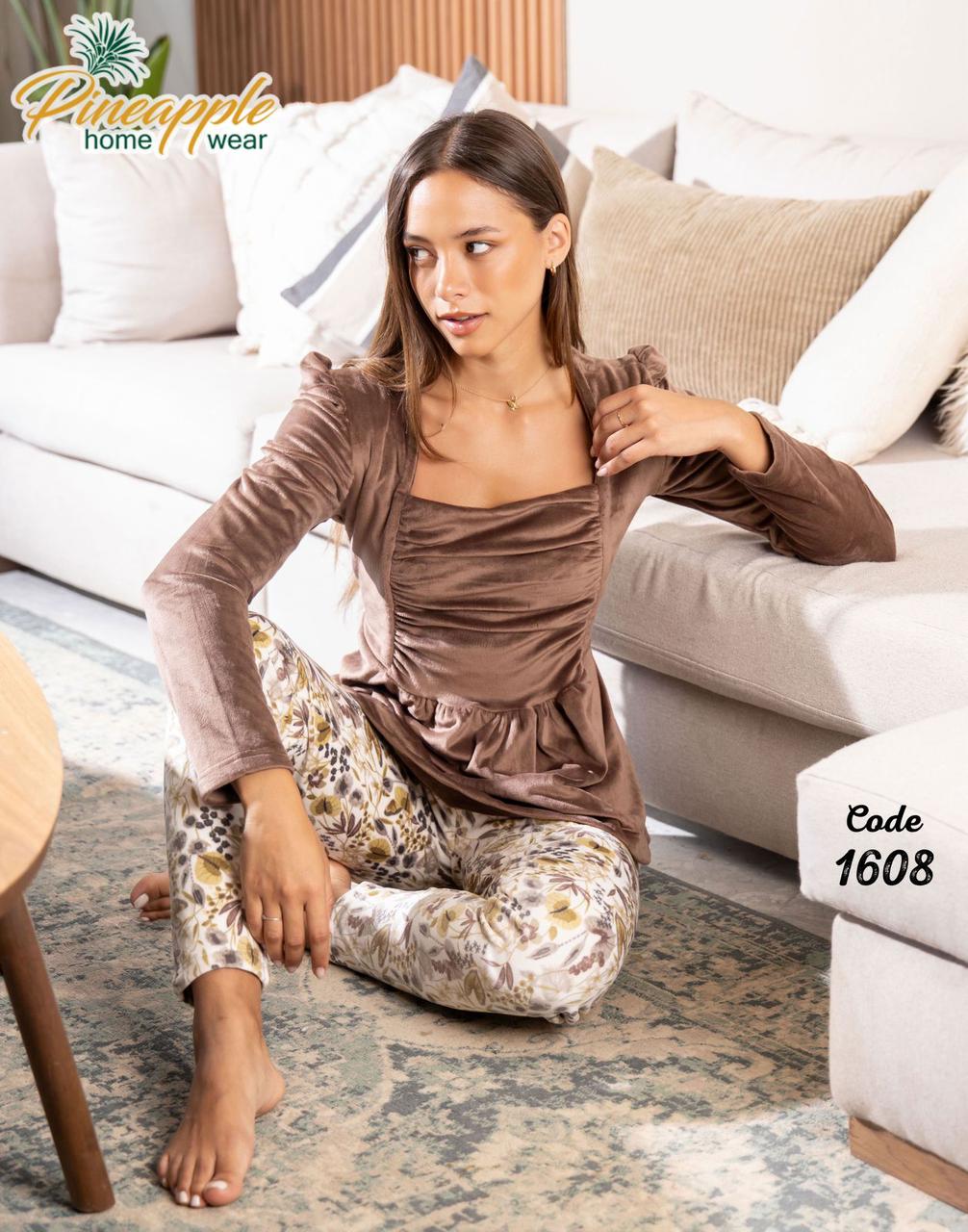 Woman sitting on a couch wearing a brown top and patterned pants with 'Pineapple Home Wear' branding.