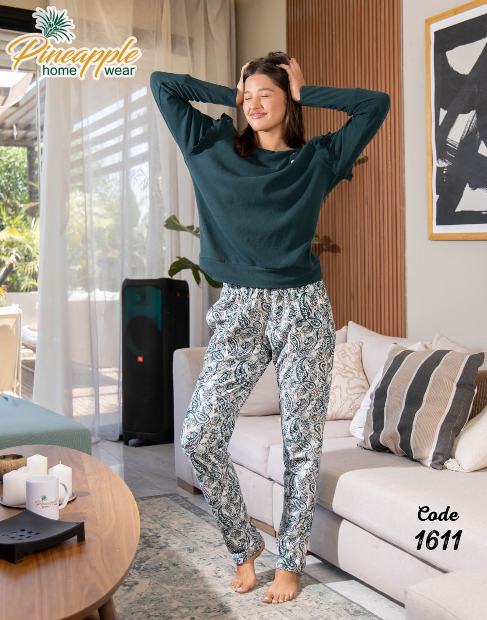 Woman in a living room wearing a teal top and patterned pants with 'Pineapple Home Wear' branding.