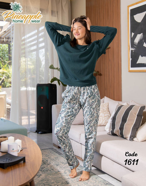 Woman in a living room wearing a teal top and patterned pants with 'Pineapple Home Wear' branding.