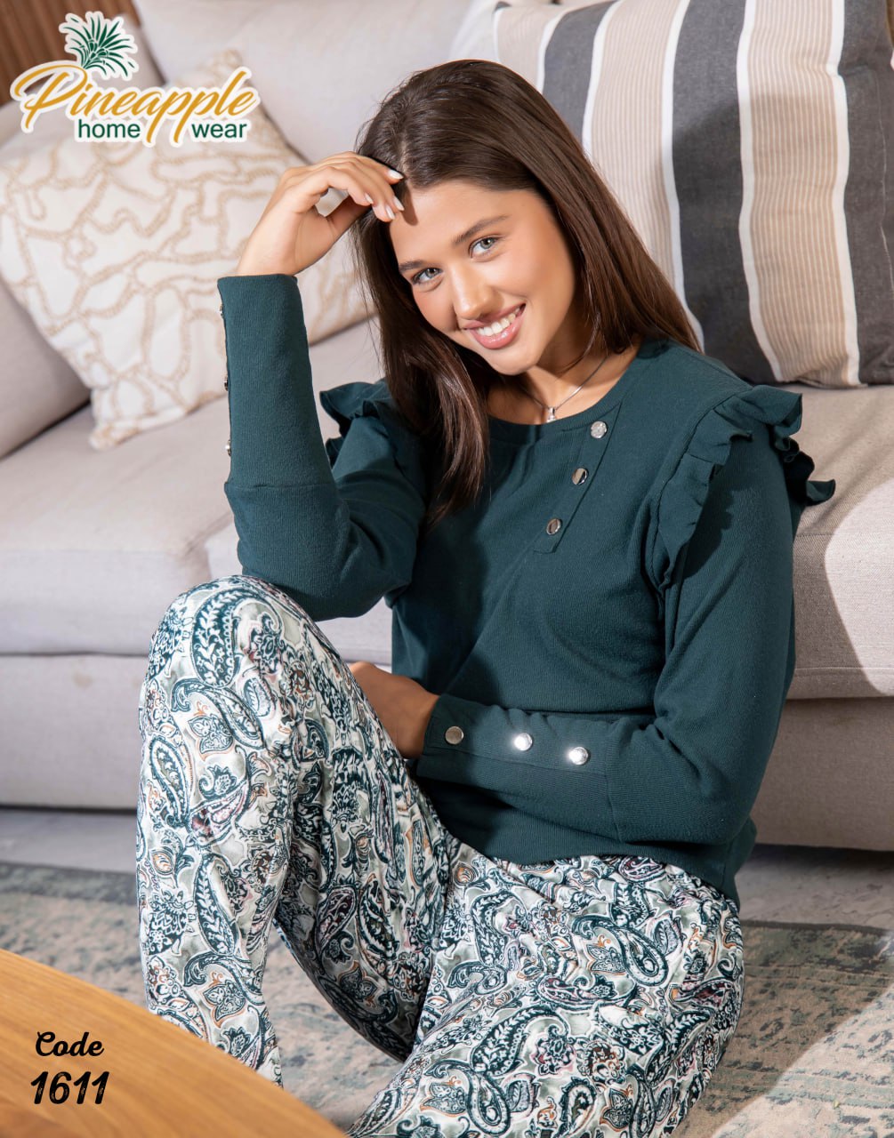 Woman sitting on a couch wearing a green top and patterned pants with 'Pineapple Home Wear' branding.