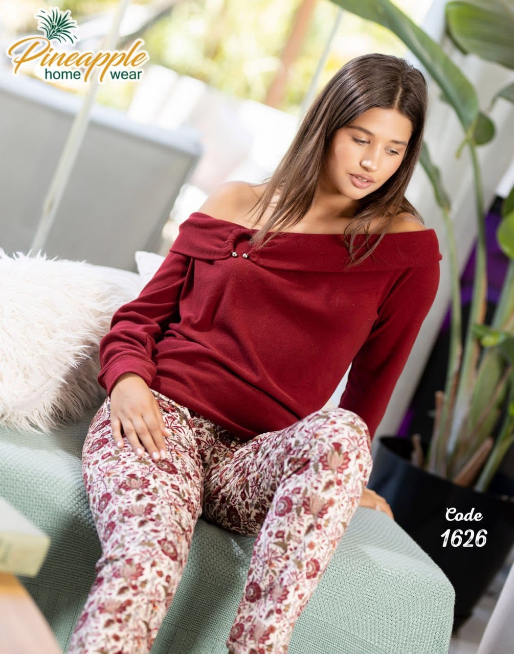 Woman wearing a red off-shoulder top and patterned pants sitting on a couch with 'Pineapple Home Wear' branding.