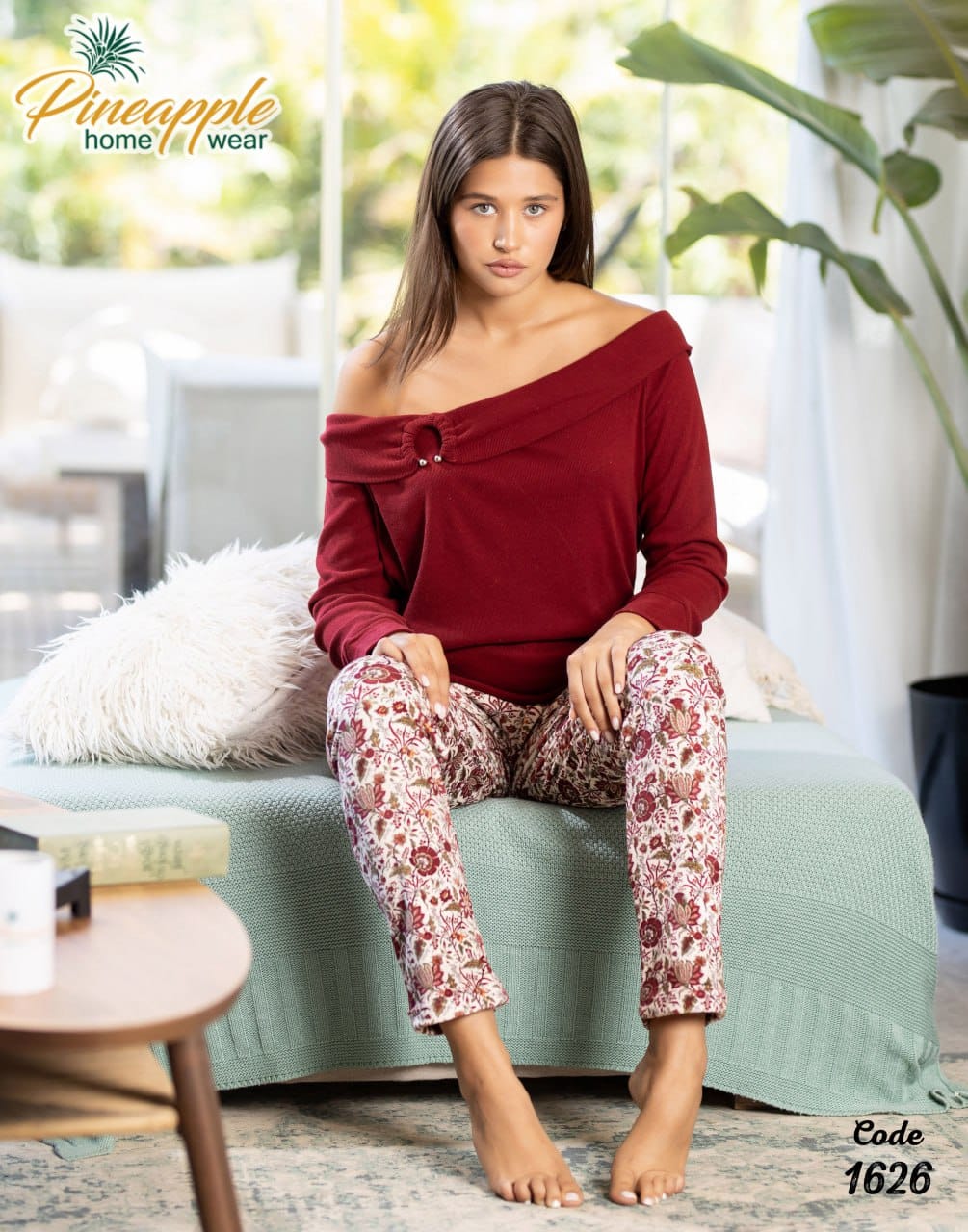 Woman wearing a red top and floral pants sitting on a couch with 'Pineapple Home Wear' branding.