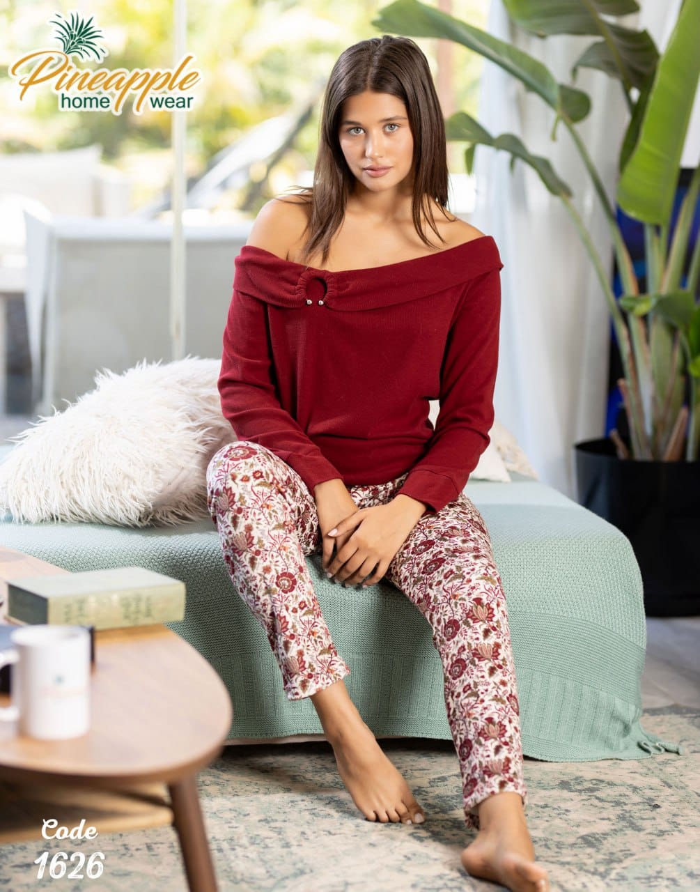 Woman sitting on a couch wearing a red top and patterned pants in a home setting.