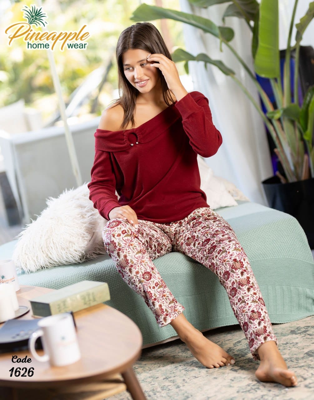 Woman sitting on a couch wearing a red top and patterned pants, with 'Pineapple Home Wear' branding.