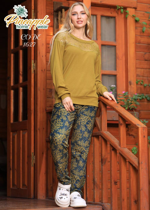 Woman wearing a yellow sweater and patterned pants standing on a wooden porch with 'Pineapple Home Wear' branding.