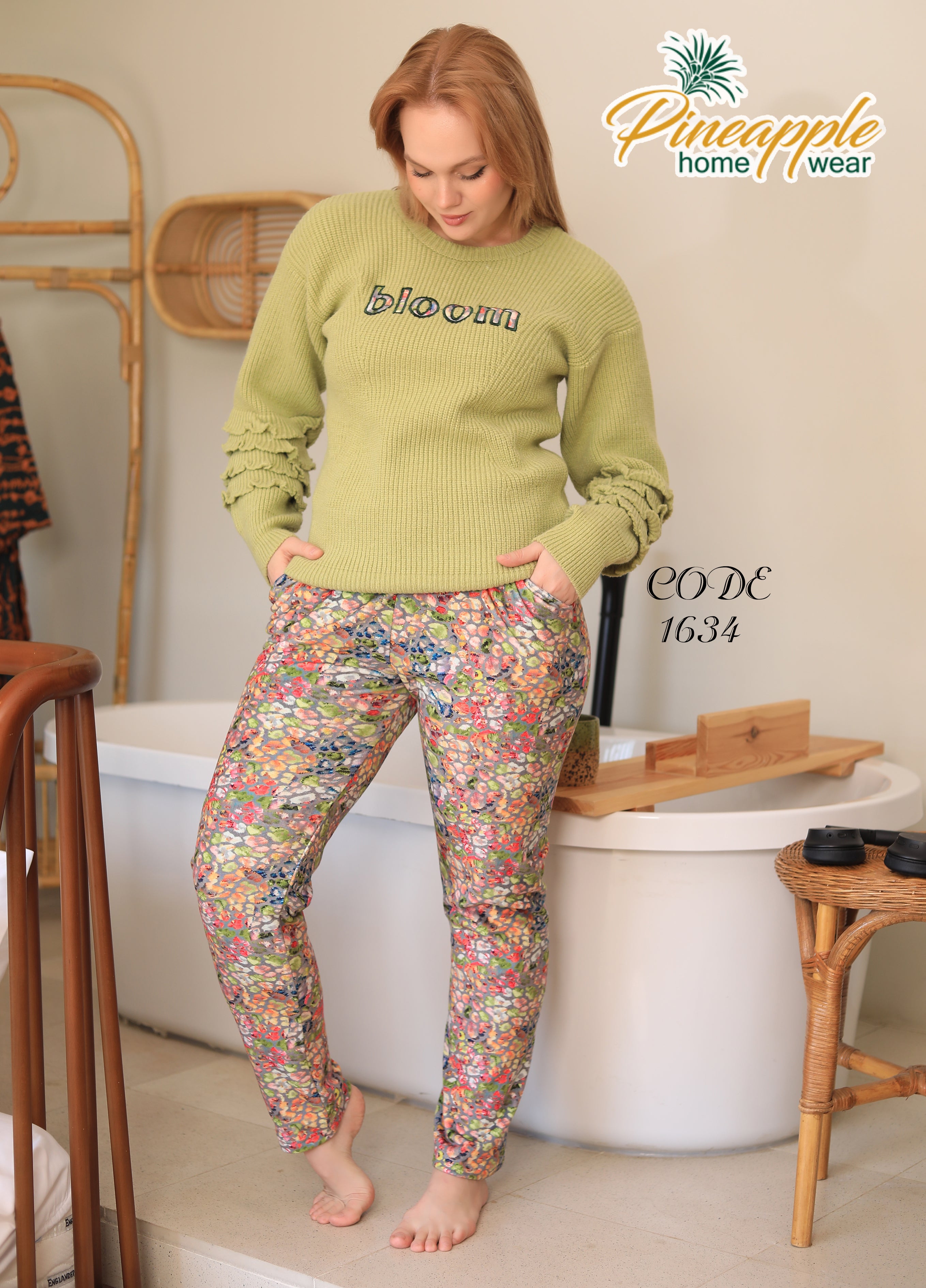 Woman wearing a green sweater and floral pants in a home setting with 'Pineapple Home Wear' branding.