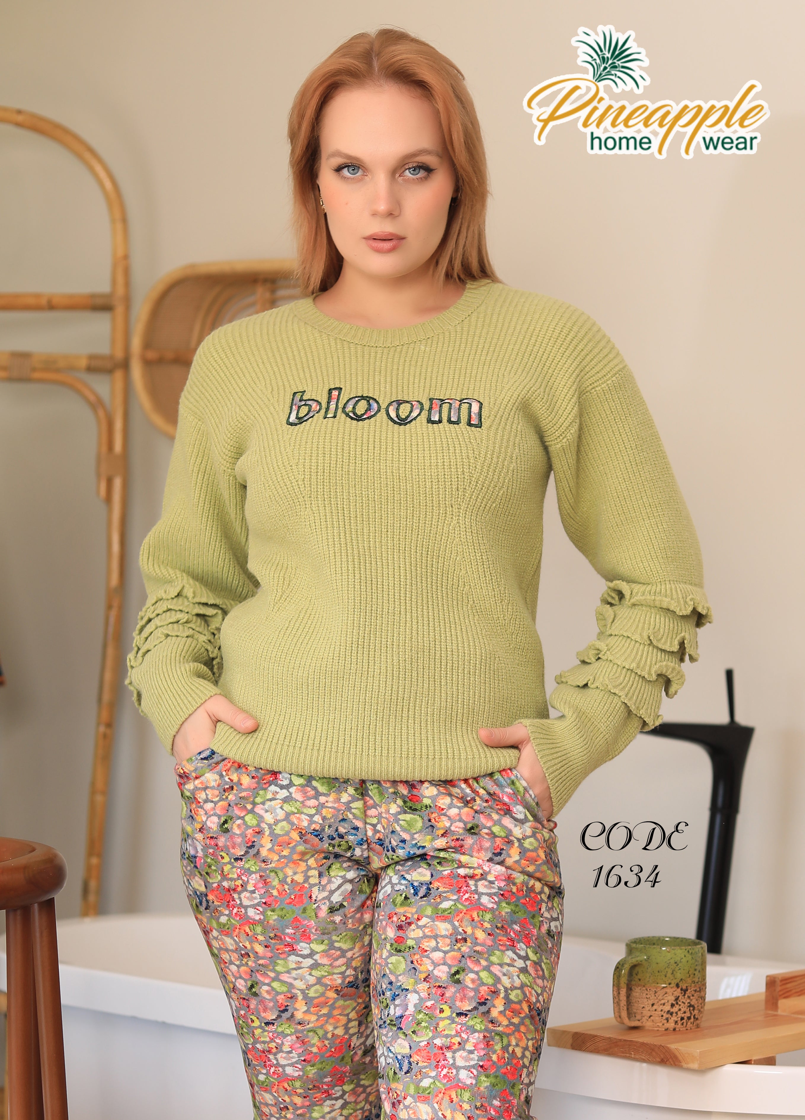 Woman wearing a green sweater with 'bloom' text and floral pants, standing in a home setting.