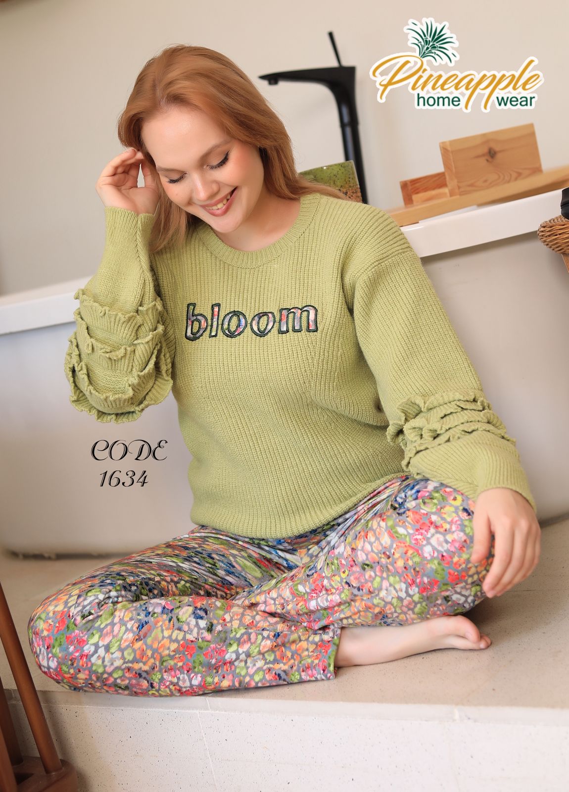 Woman wearing a green 'bloom' sweater sitting on a couch with a colorful patterned cushion.