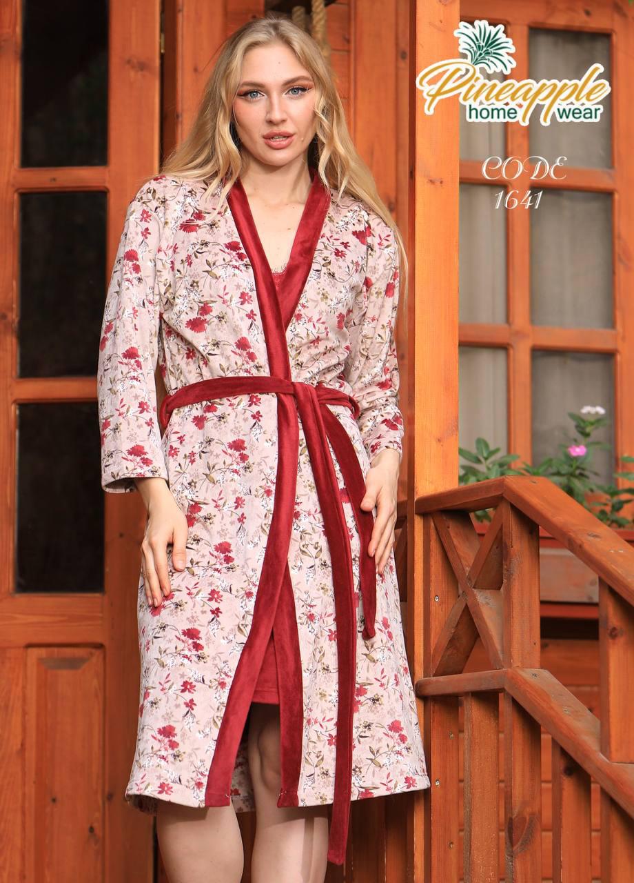 Woman wearing a floral robe with a red belt standing in front of a wooden door.