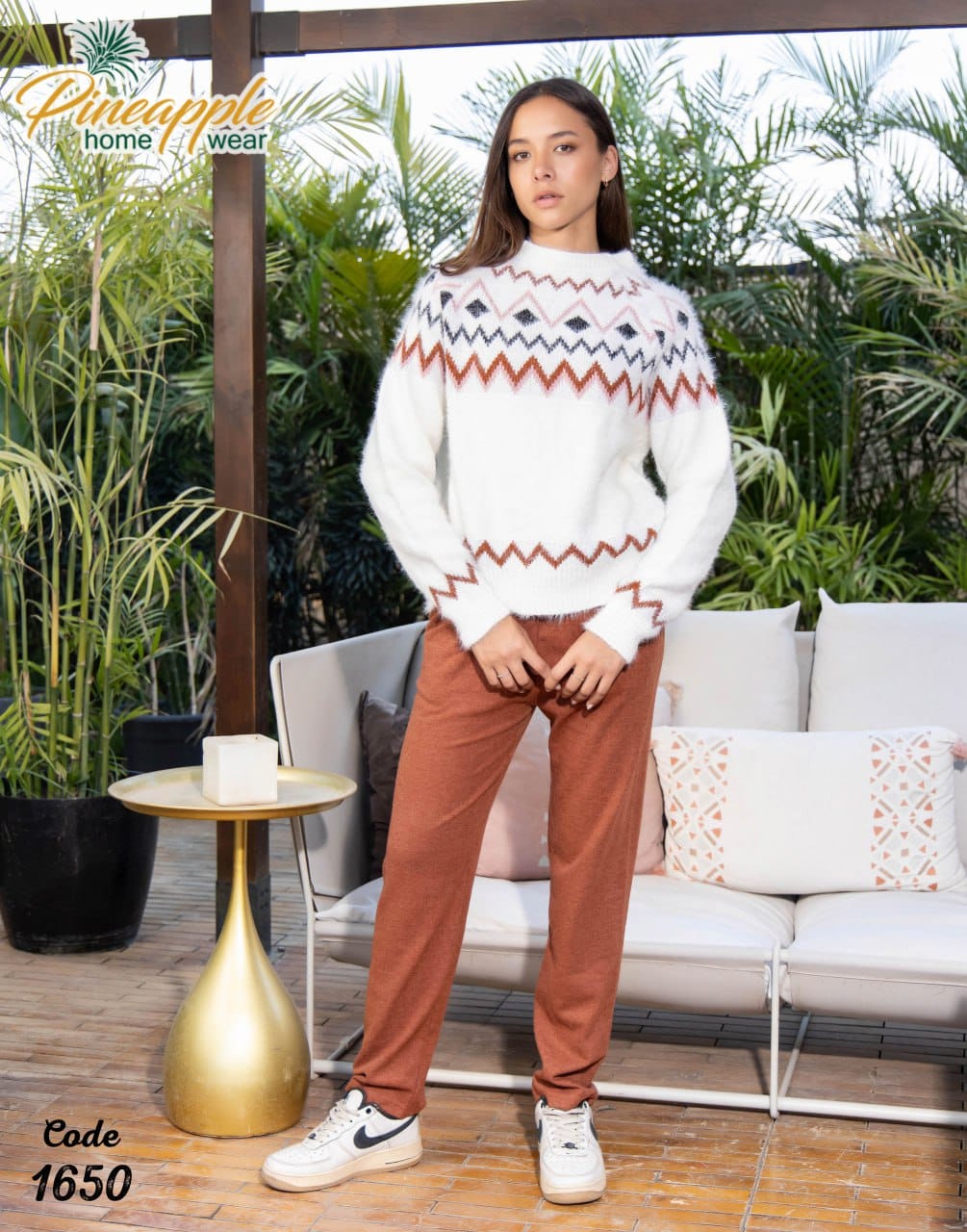 Woman wearing a patterned sweater and brown pants standing in an outdoor setting with 'Pineapple Home Wear' branding.