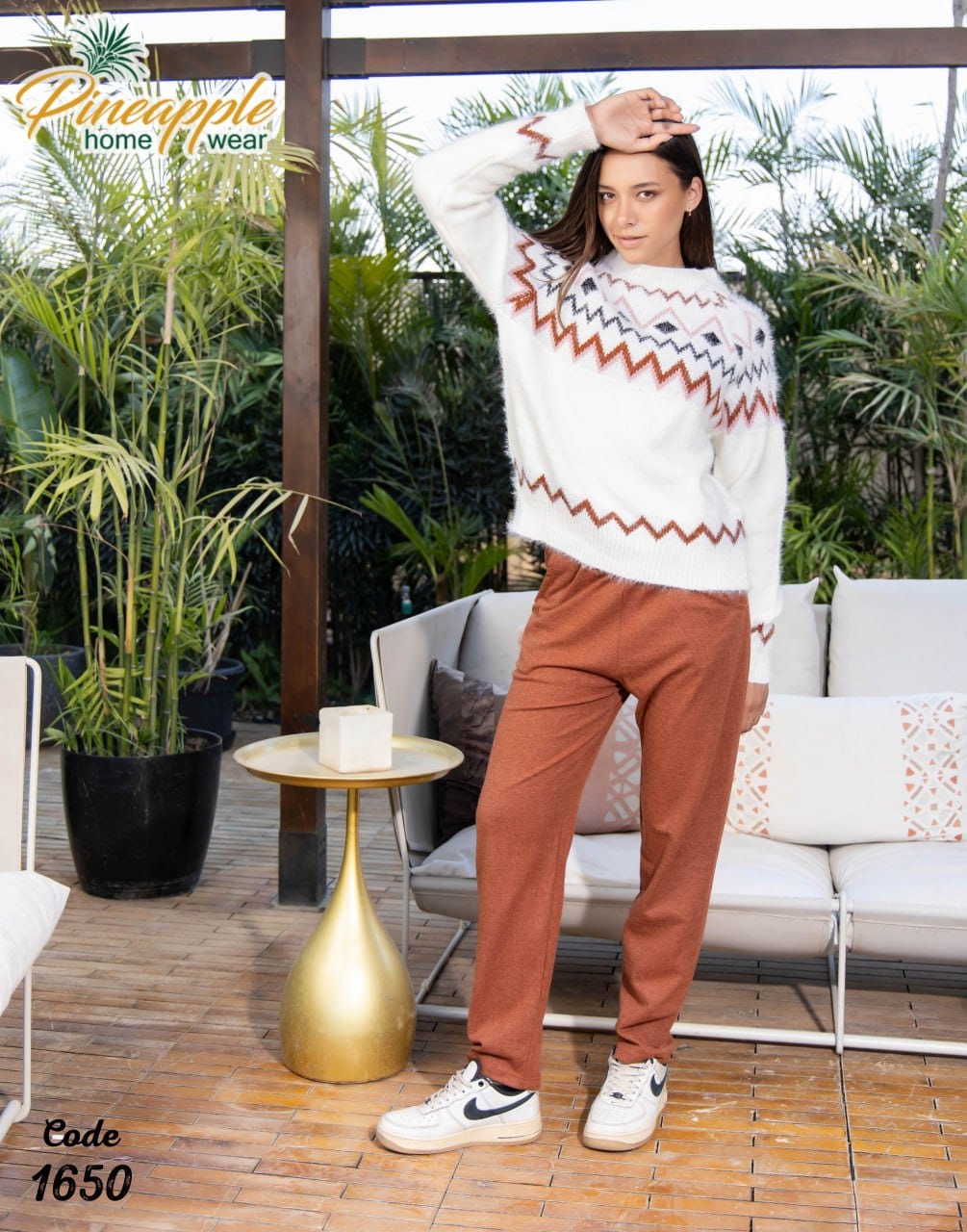 Woman wearing a white sweater with red and blue patterns and brown pants standing on a patio.