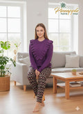 Woman wearing a purple sweater and patterned pants sitting on a couch in a bright living room with 'Pineapple Home Wear' branding.
