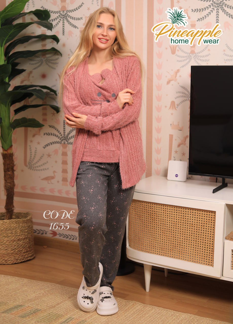 Woman wearing a pink cardigan and gray pants standing in a room with a television and decorative wall.