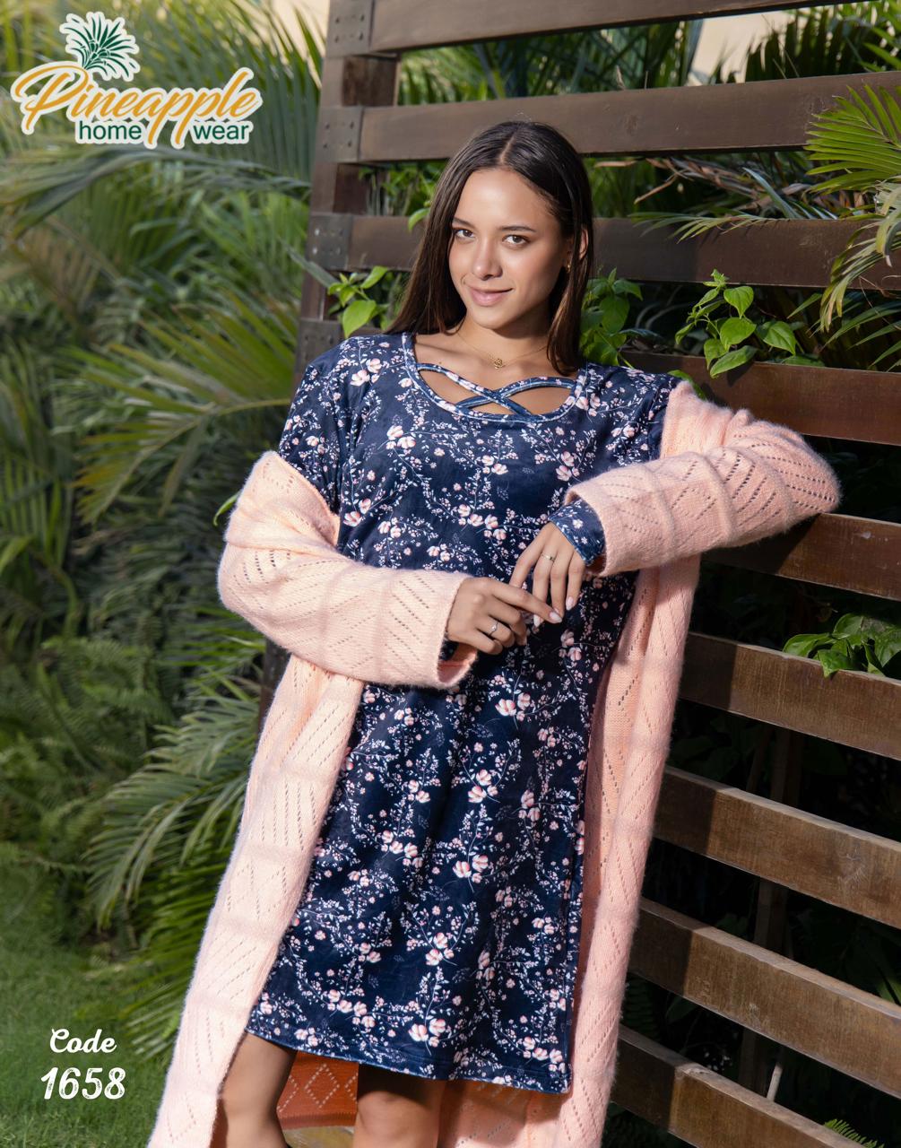Woman wearing a navy floral dress with a pink cardigan against a wooden and green leafy background, branded 'Pineapple Home Wear'.