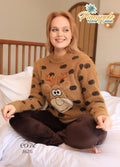 Woman wearing a brown sweater with a reindeer design sitting on a bed, branded 'Pineapple Home Wear'.