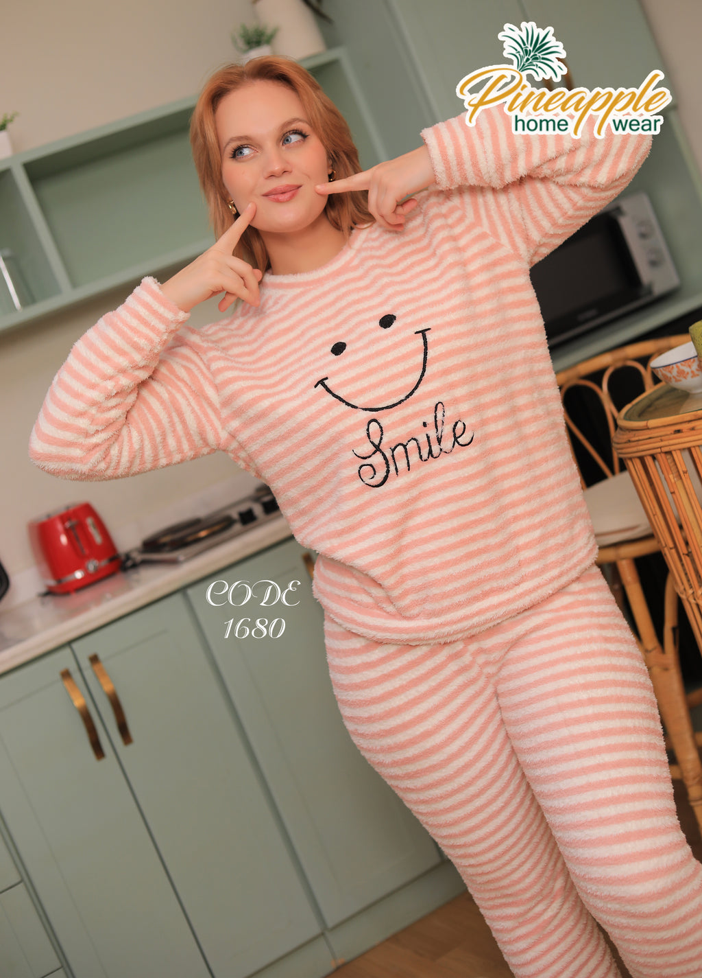 Woman wearing pink striped pajamas with a smiley face design in a kitchen.