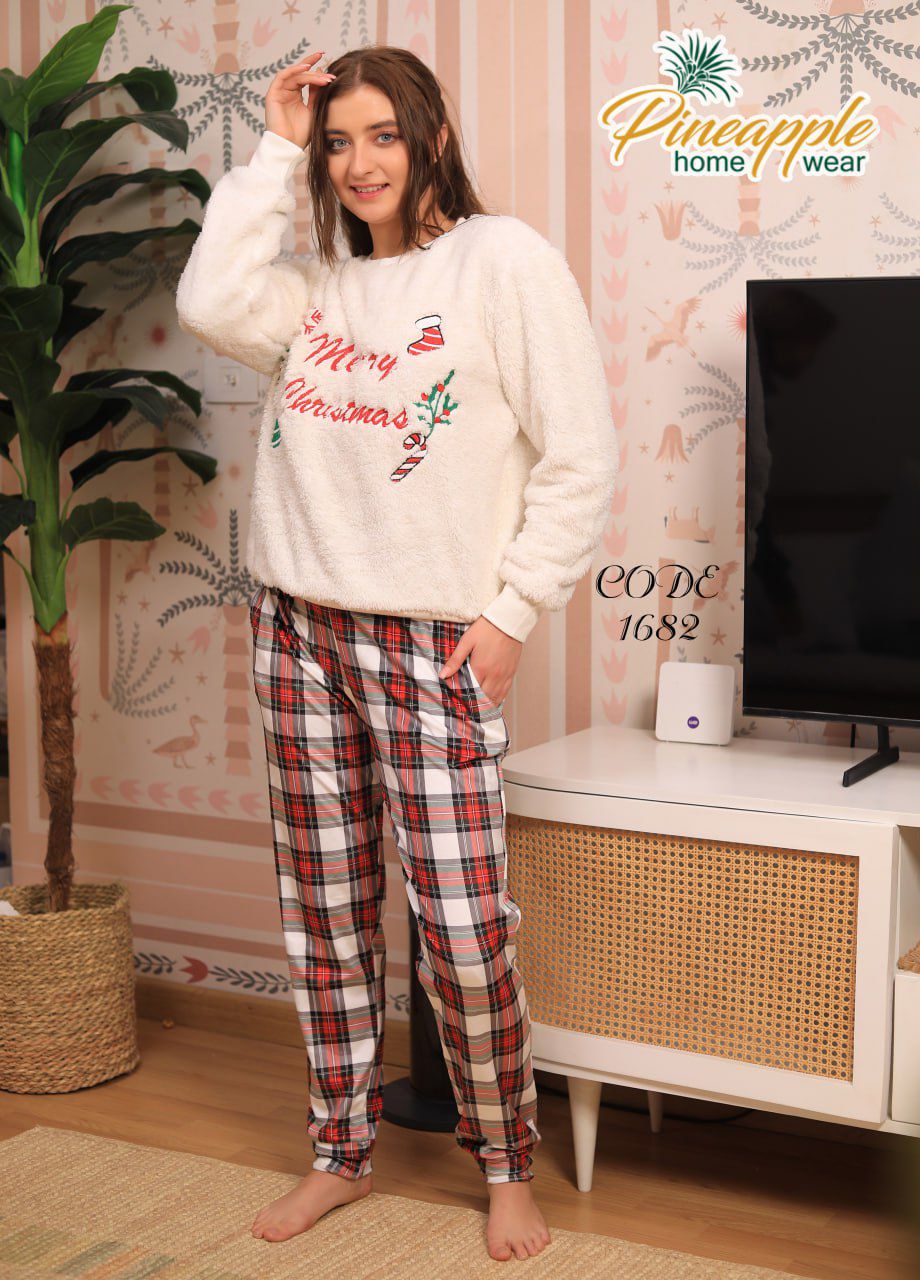 Woman wearing a white Christmas-themed sweater and plaid pants in a room with a TV and plant.