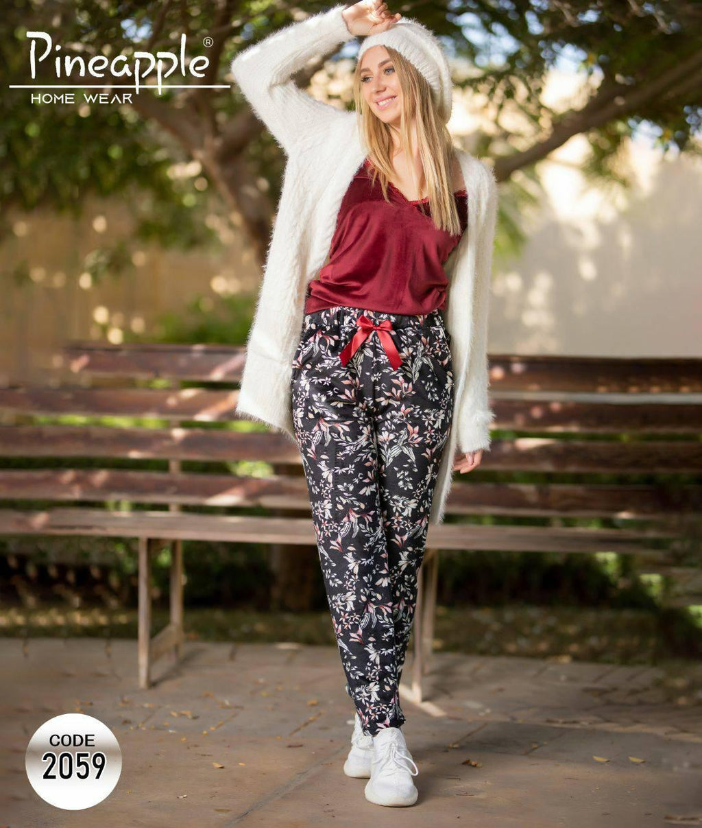 Woman wearing a white cardigan, red top, and floral pants with a red ribbon outdoors.