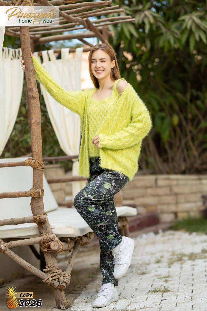 Woman wearing a bright green cardigan and patterned pants sitting on a wooden bench outdoors.