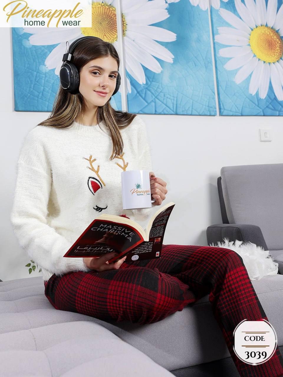 Woman in festive pajamas reading a book with headphones on, sitting on a couch.