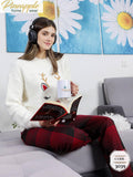 Woman in festive pajamas reading a book with headphones on, sitting on a couch.