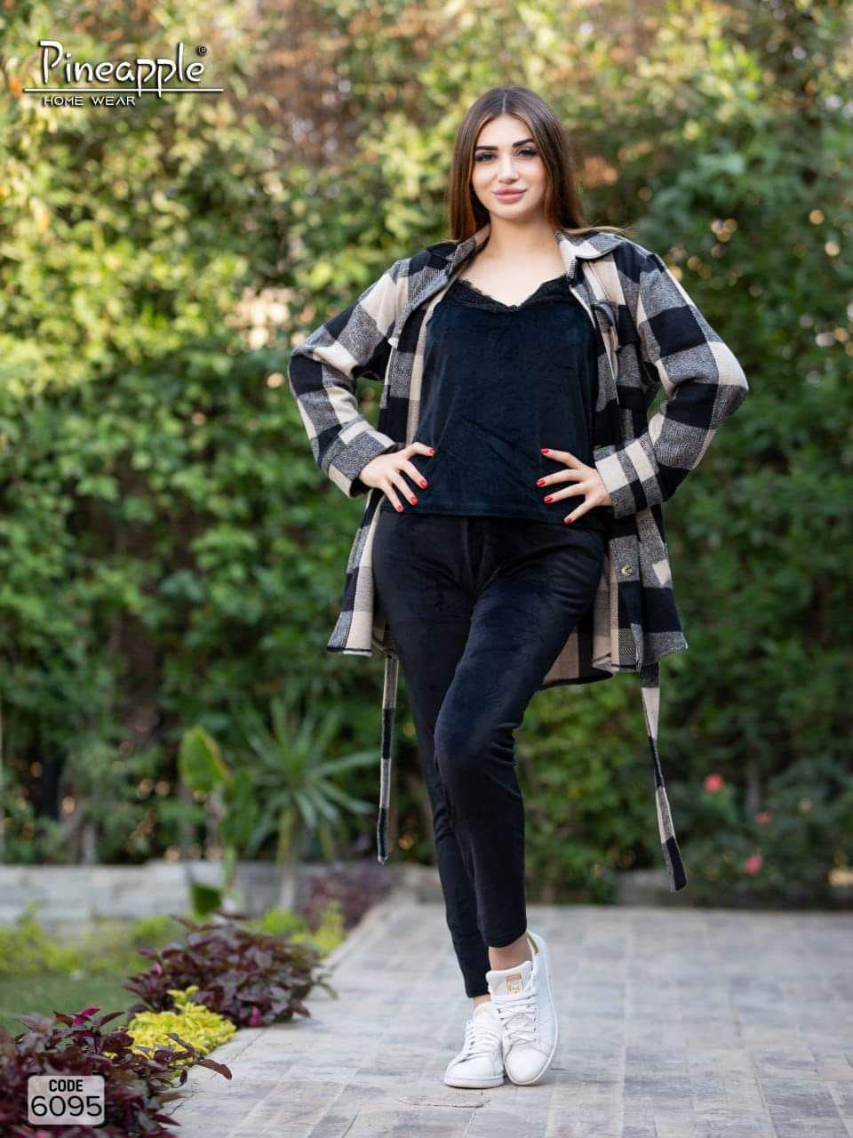 Woman wearing a checkered shirt over a black top and pants, standing outdoors with greenery in the background.