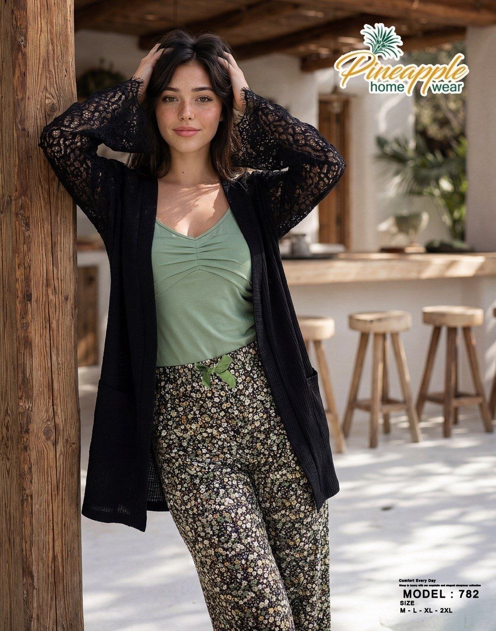 Woman wearing a green top and floral pants with a black cardigan, standing in a casual setting.