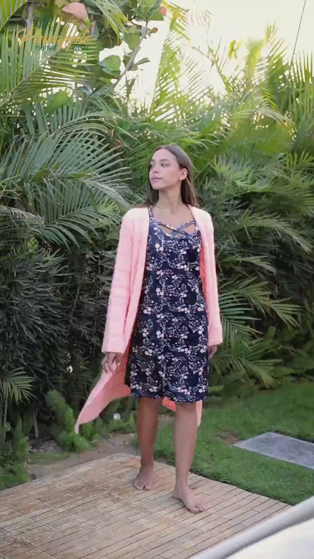 Woman wearing a navy floral dress with a pink cardigan against a green leafy background, branded 'Pineapple Home Wear'.