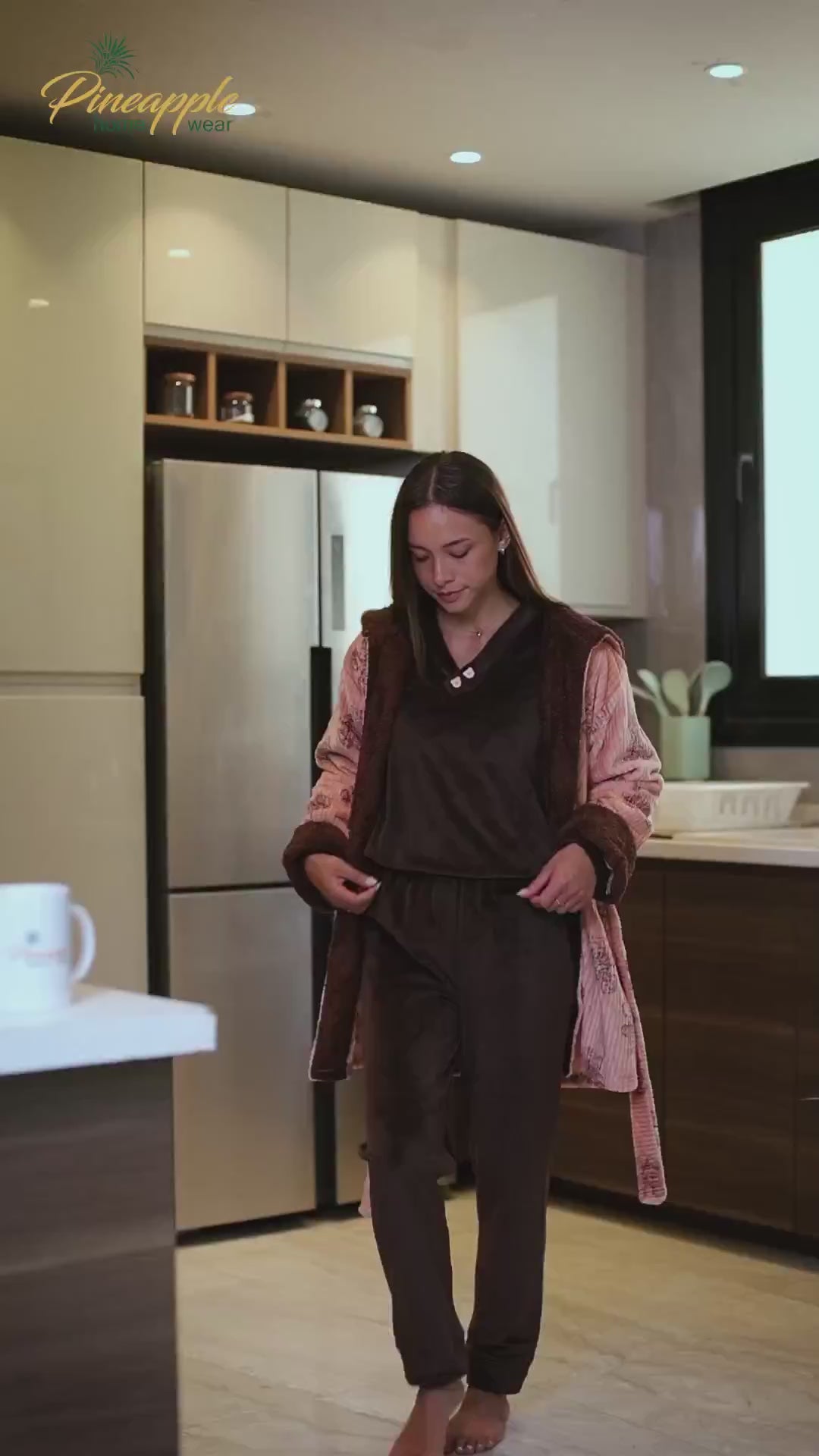 Woman wearing a patterned robe in a home setting with 'Pineapple Home Wear' branding.