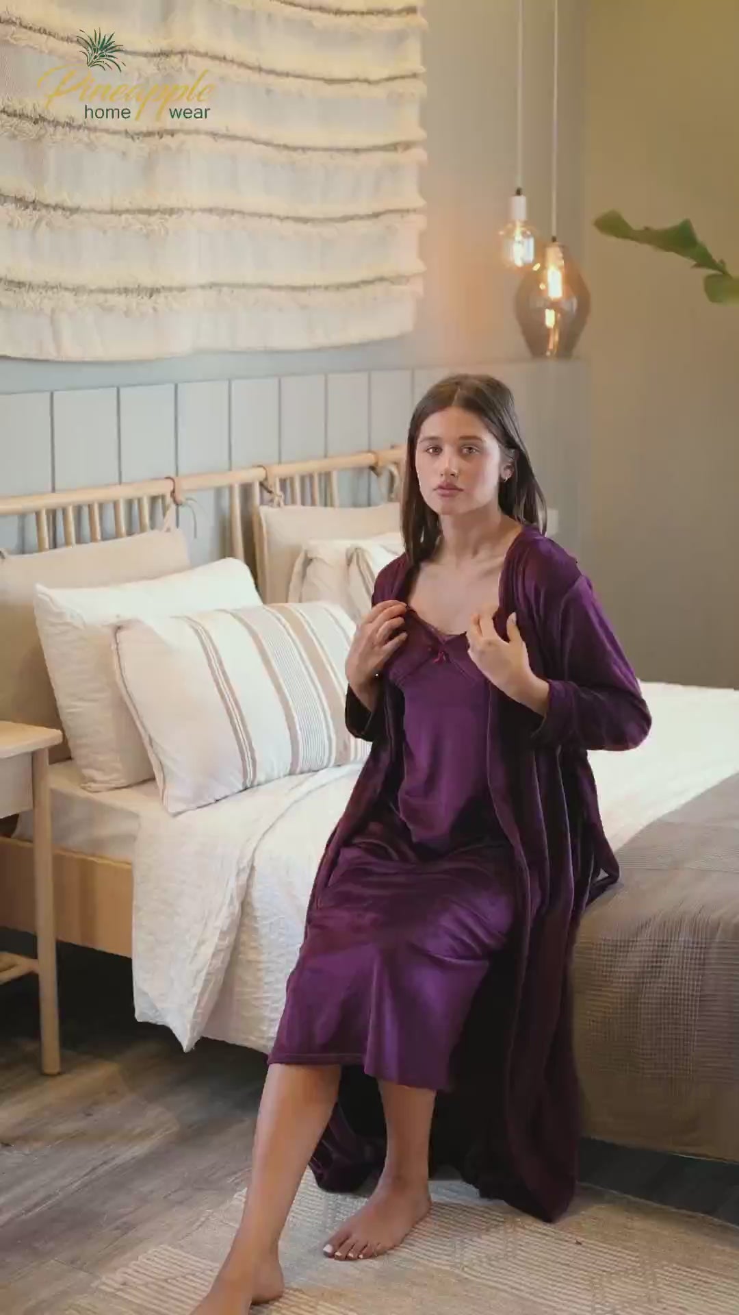 Woman wearing a purple robe with lace details in a bedroom setting, branded 'Pineapple Home Wear'.