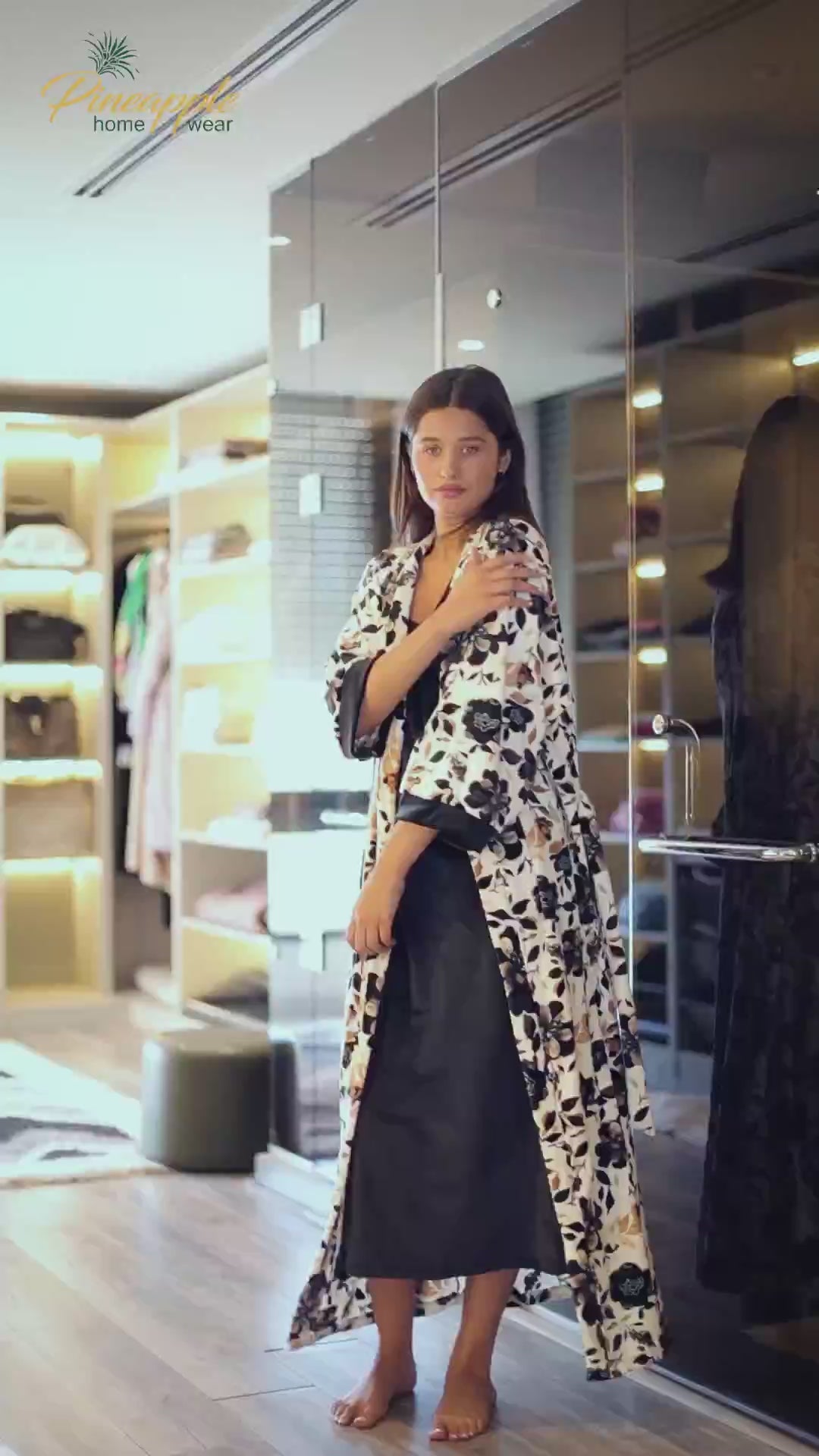 Woman wearing a black slip dress with a patterned robe in an indoor setting, with 'Pineapple Home Wear' branding.
