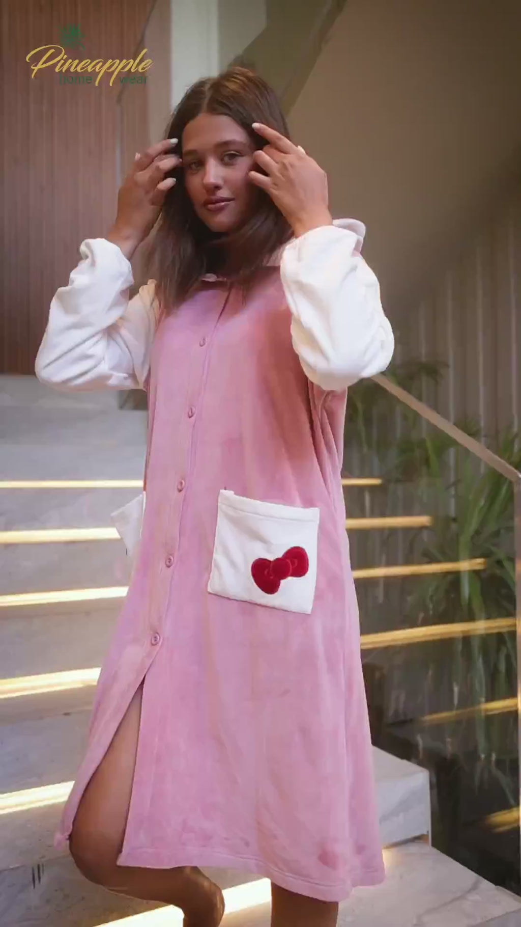 Woman wearing a pink shark-themed robe in a home setting with 'Pineapple Home Wear' branding.