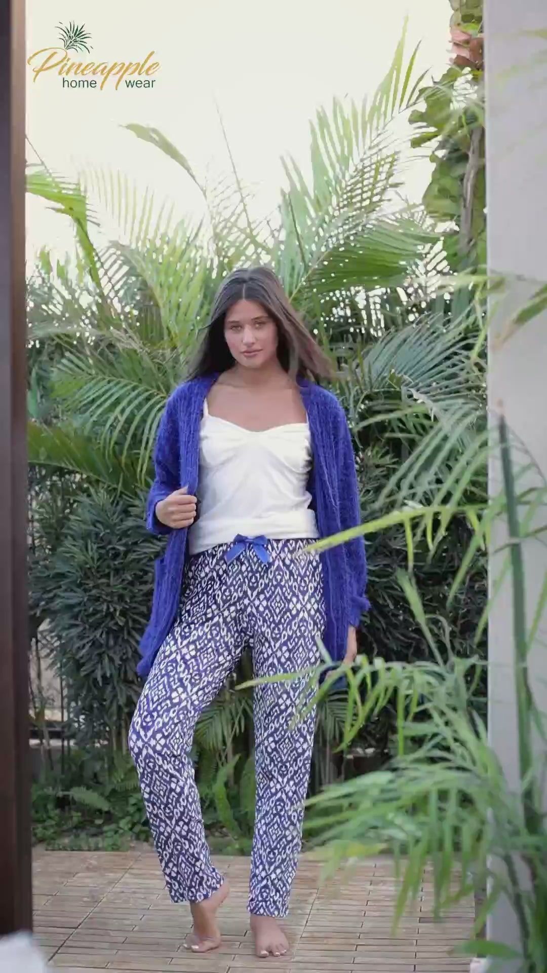 Woman wearing a blue cardigan and white top sitting on a couch with 'Pineapple Home Wear' branding.
