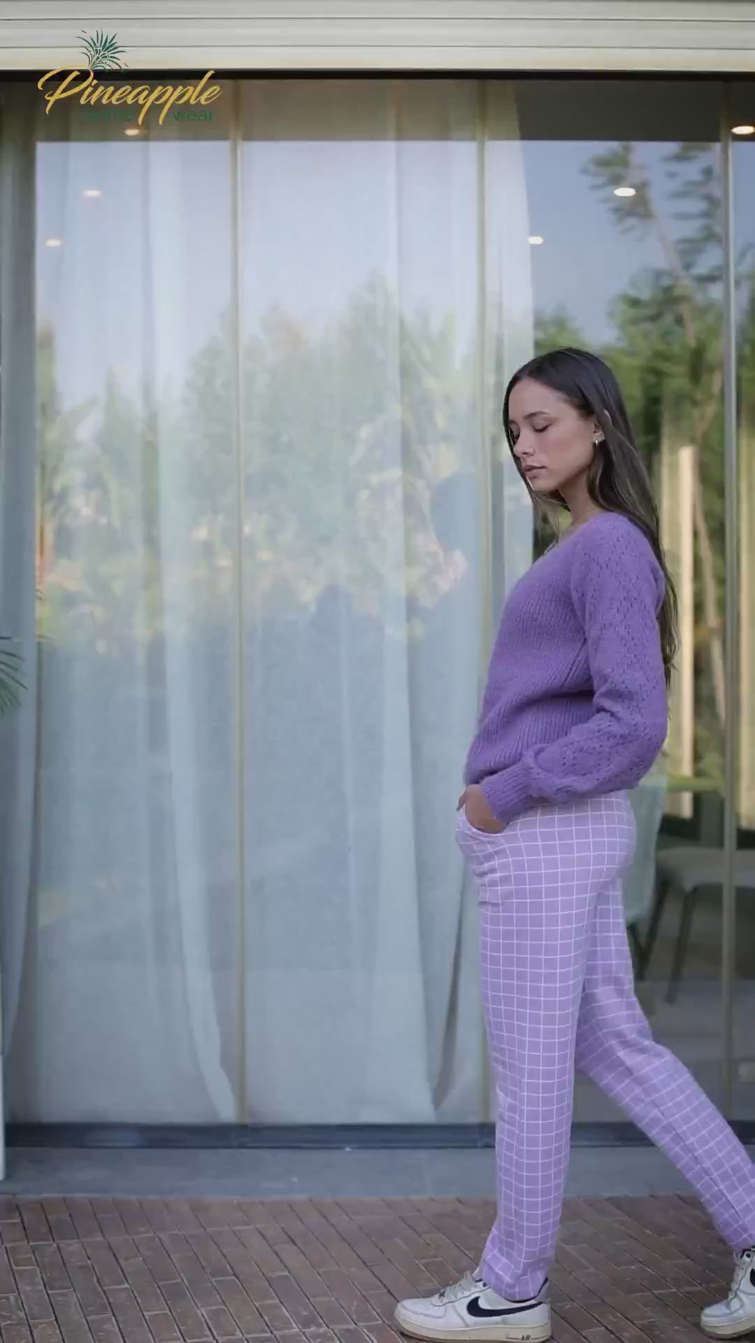Woman wearing a purple sweater and checkered pants outdoors, with 'Pineapple Home Wear' branding.