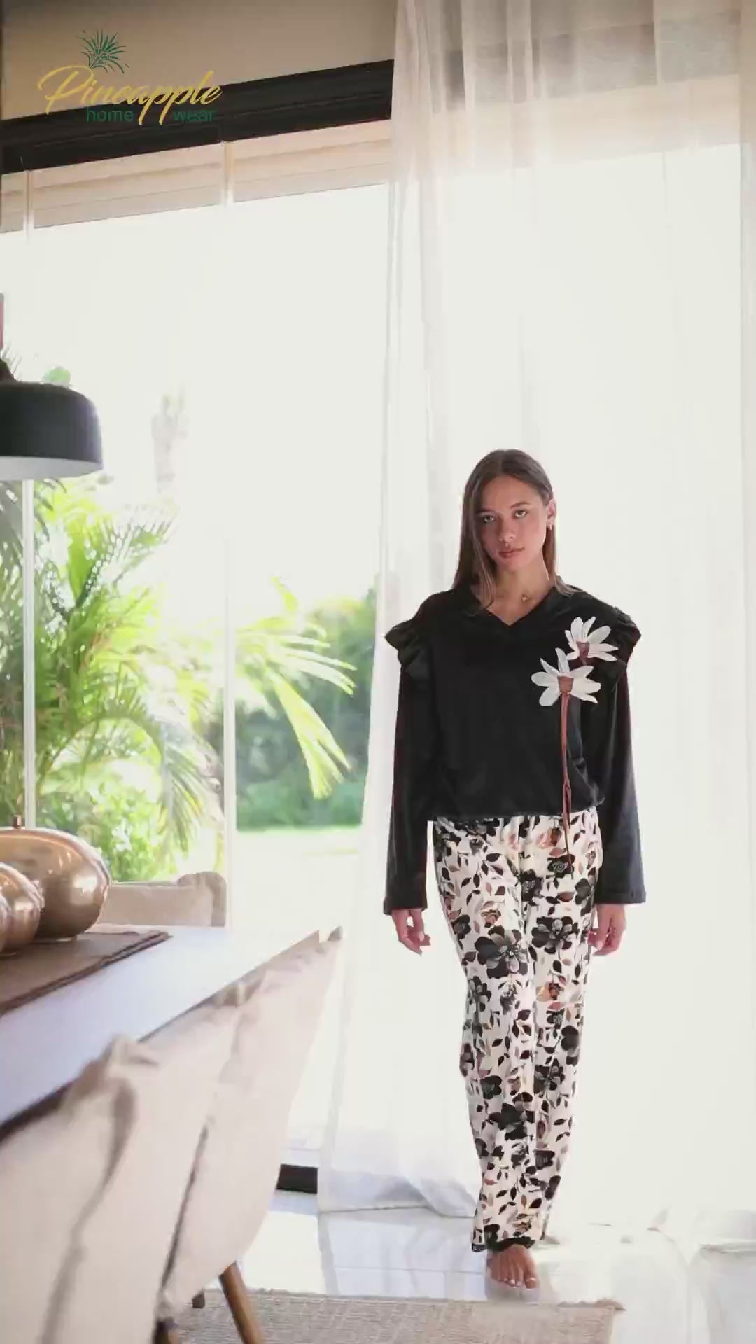 Woman wearing a black top with floral details and patterned pants, with 'Pineapple Home Wear' logo.