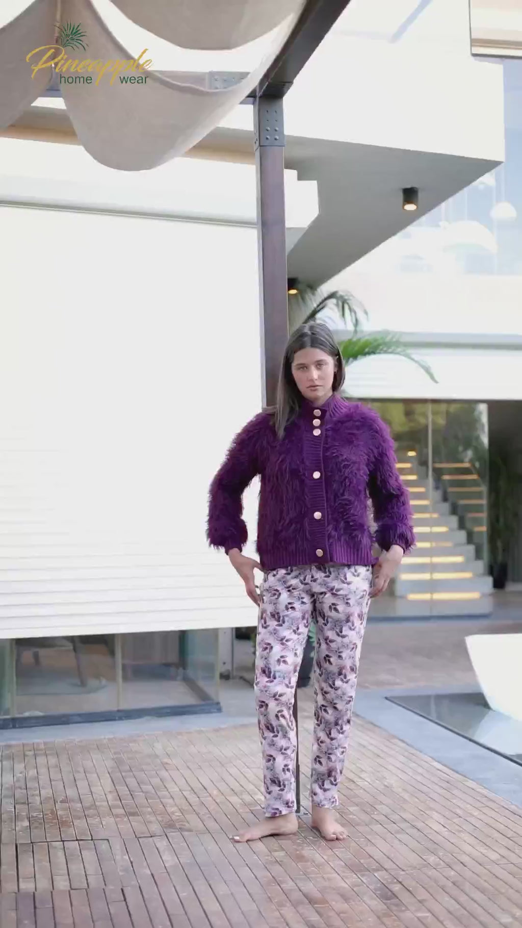 Woman wearing a purple cardigan and patterned pants standing in an outdoor setting with 'Pineapple Home Wear' branding.