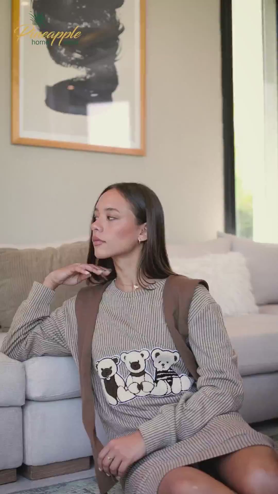 Woman wearing a beige ribbed dress with a graphic design in a living room setting, branded 'Pineapple Home Wear'.