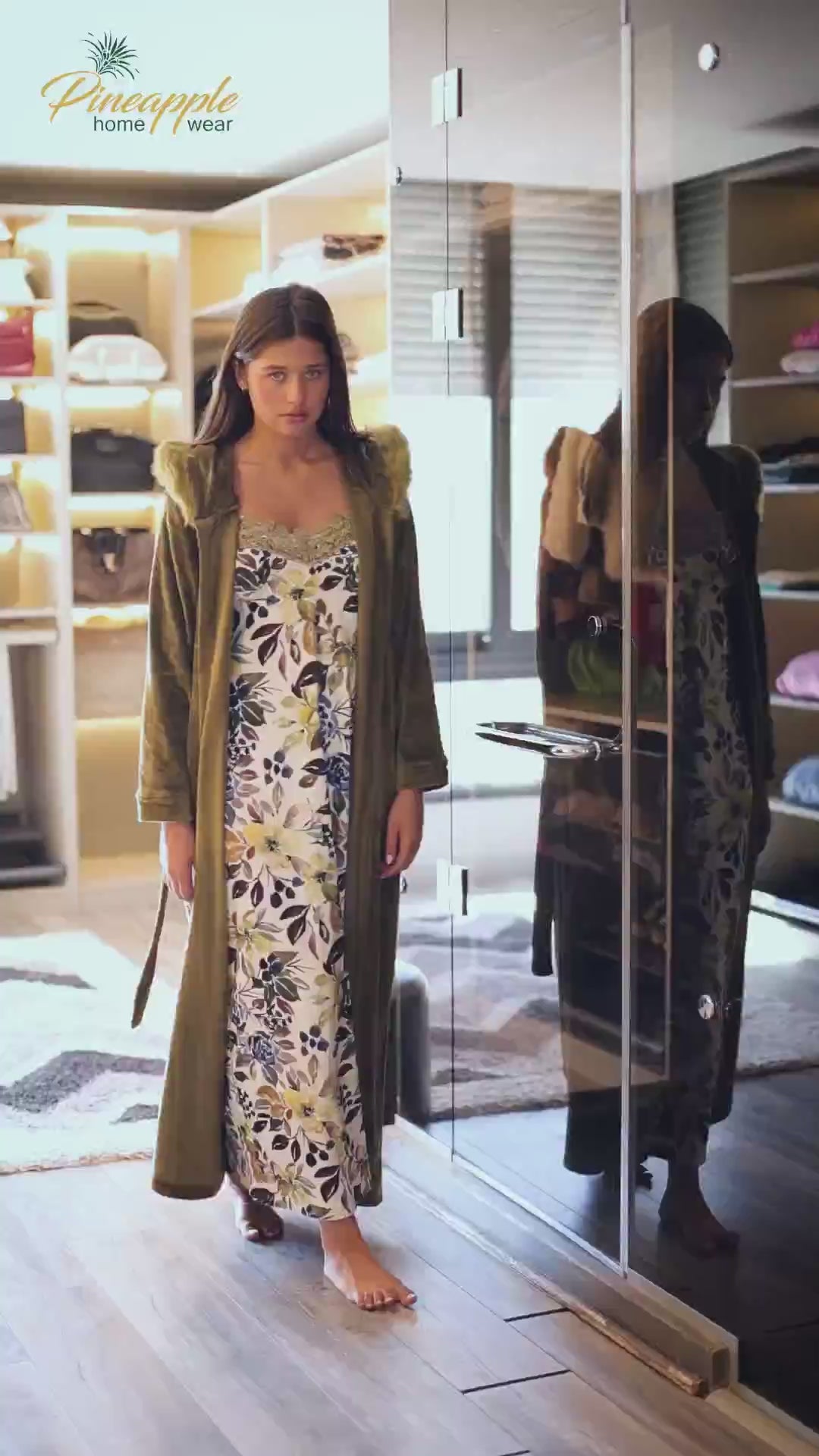 Woman wearing a floral dress under a green robe with fur trim in a store setting.