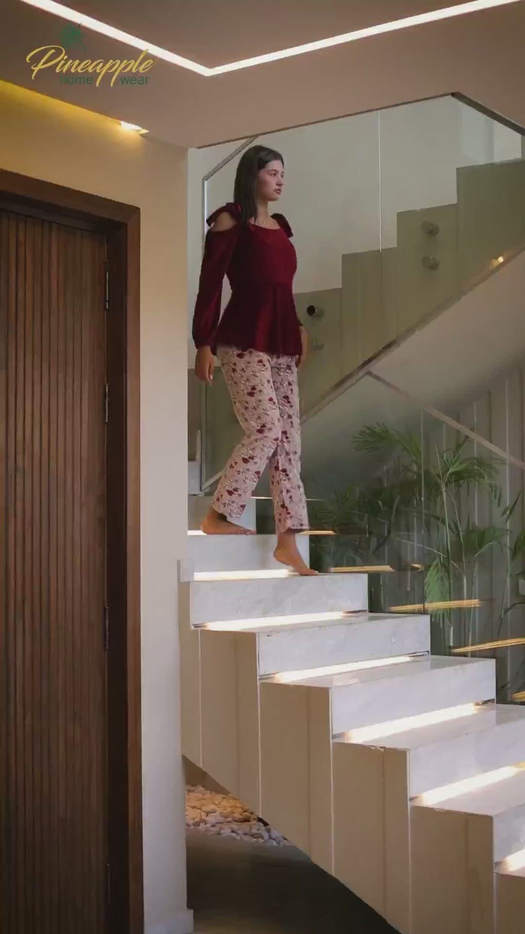Woman wearing a red top and floral pants in a living room setting with 'Pineapple Home Wear' branding.