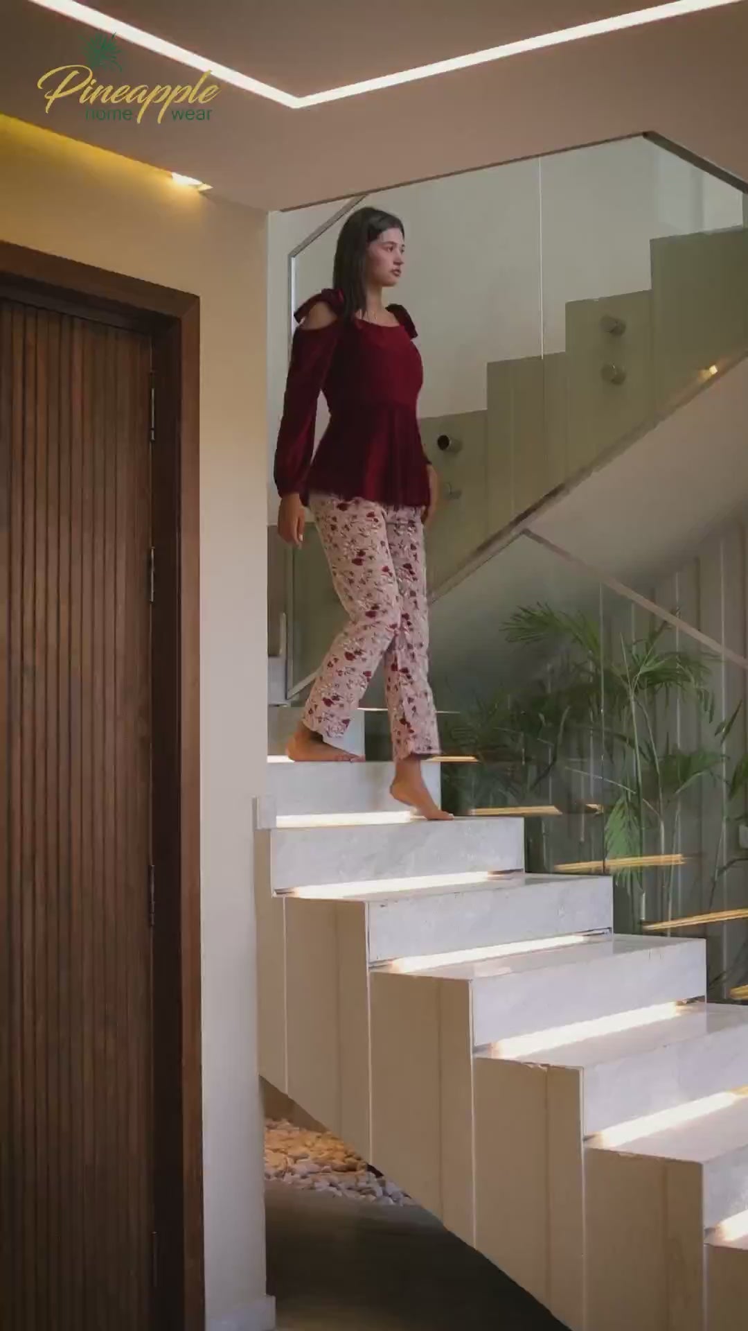Woman wearing a red top and floral pants in a living room setting with 'Pineapple Home Wear' branding.